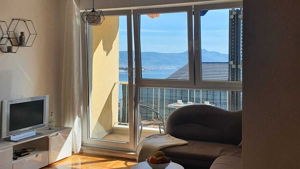 A modern living room with a large window, a flat-screen TV, a sofa, and a small coffee table. - Romantic comfortable apartment (Trogir)