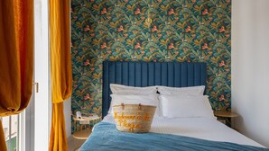 Ein Schlafzimmer mit einem blauen Kopfteil, einem Bett mit weißen Leinen, einer blauen Decke und einem gewebten Korb mit Aufschrift.