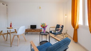 Ein modernes Wohnzimmer mit Esstisch, einer Couch, einem kleinen Beistelltisch mit einer Vase, einem Fernseher und einer Holzkommode.
