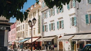 Straßenansicht mit Gebäuden, Geschäften und einem blauen Auto.