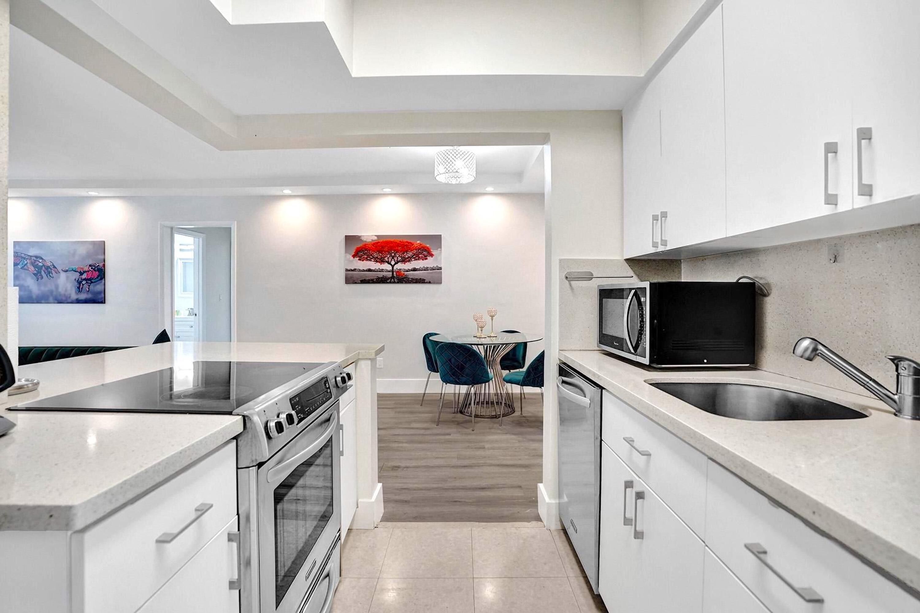 Een moderne keuken met witte kasten, een zwarte magnetron en een eethoek met turquoise stoelen.