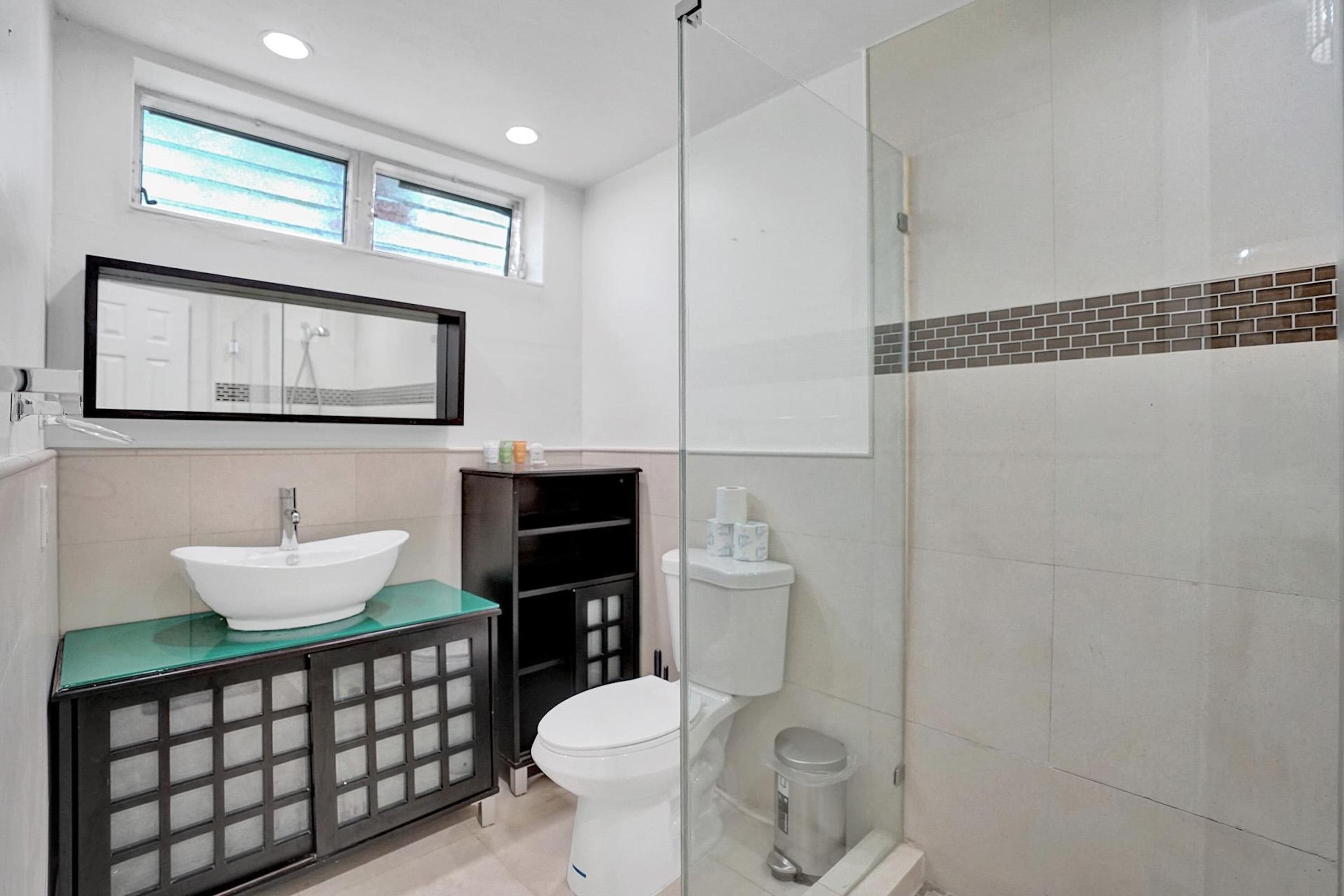 A modern bathroom with a glass-enclosed shower, a white sink with a green countertop, and a black cabinet with glass doors.