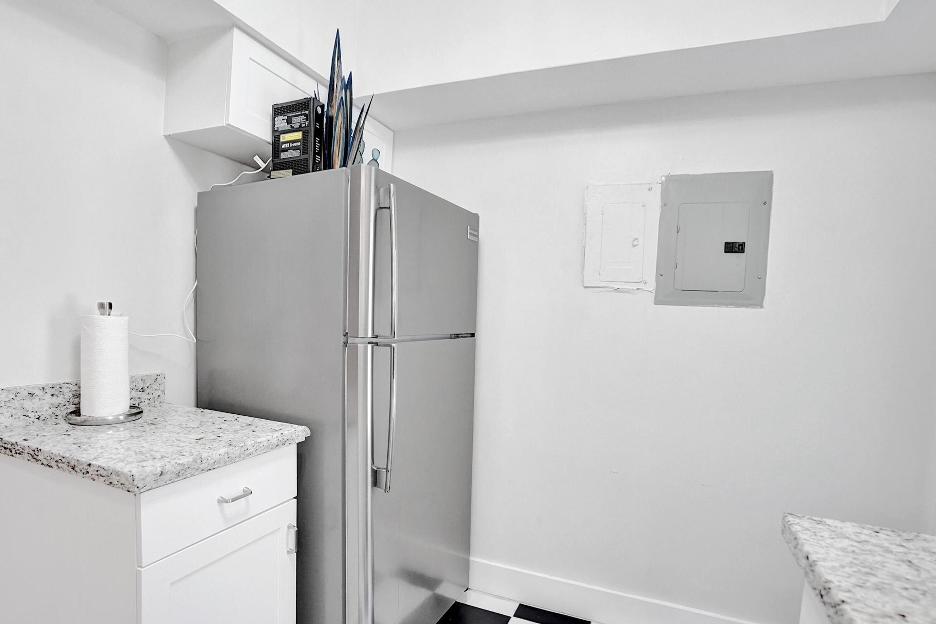 A compact kitchen with a stainless steel refrigerator, white cabinetry, and a granite countertop.
