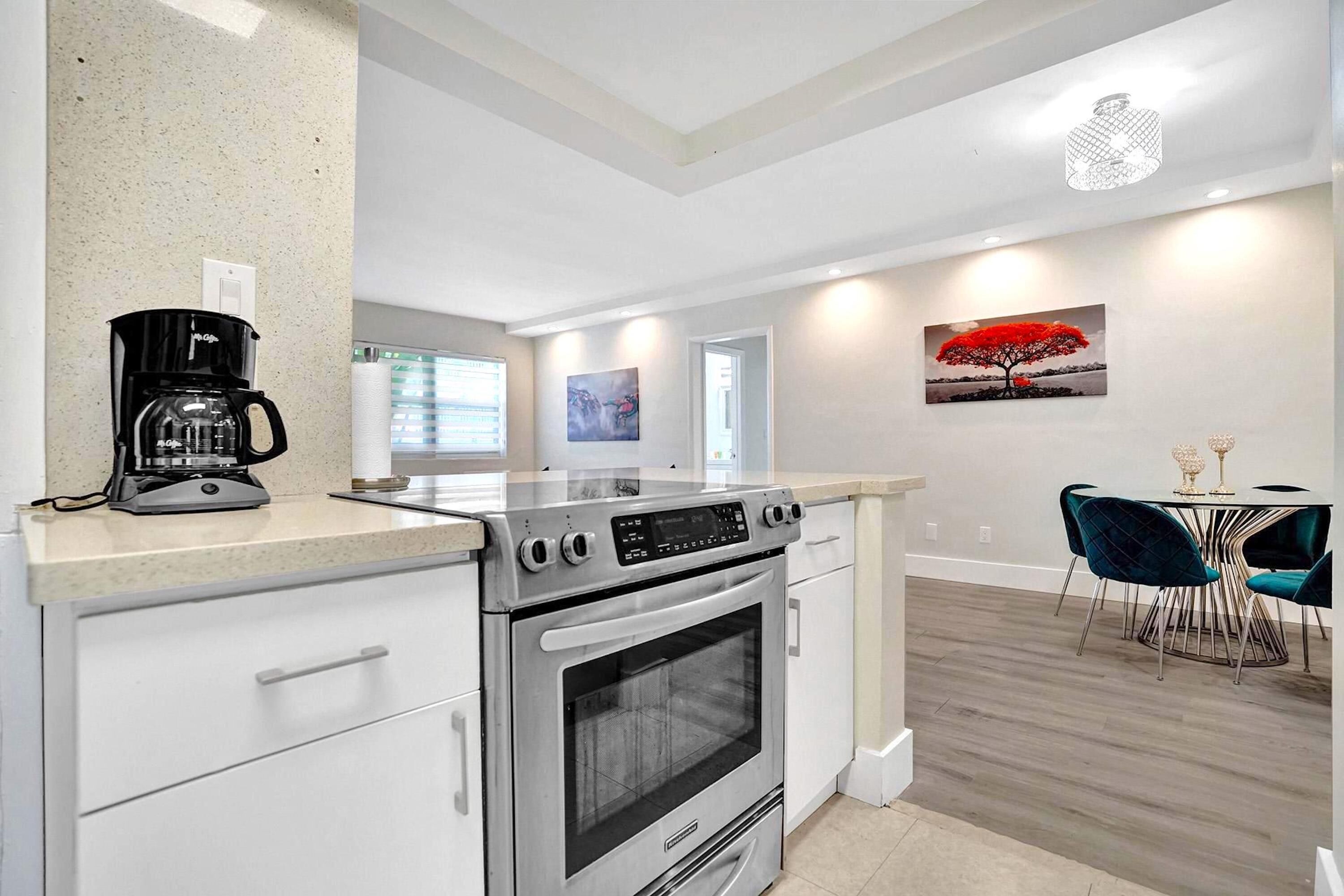 A modern kitchen with a built-in oven, a coffee maker, and a dining area with a table and chairs.