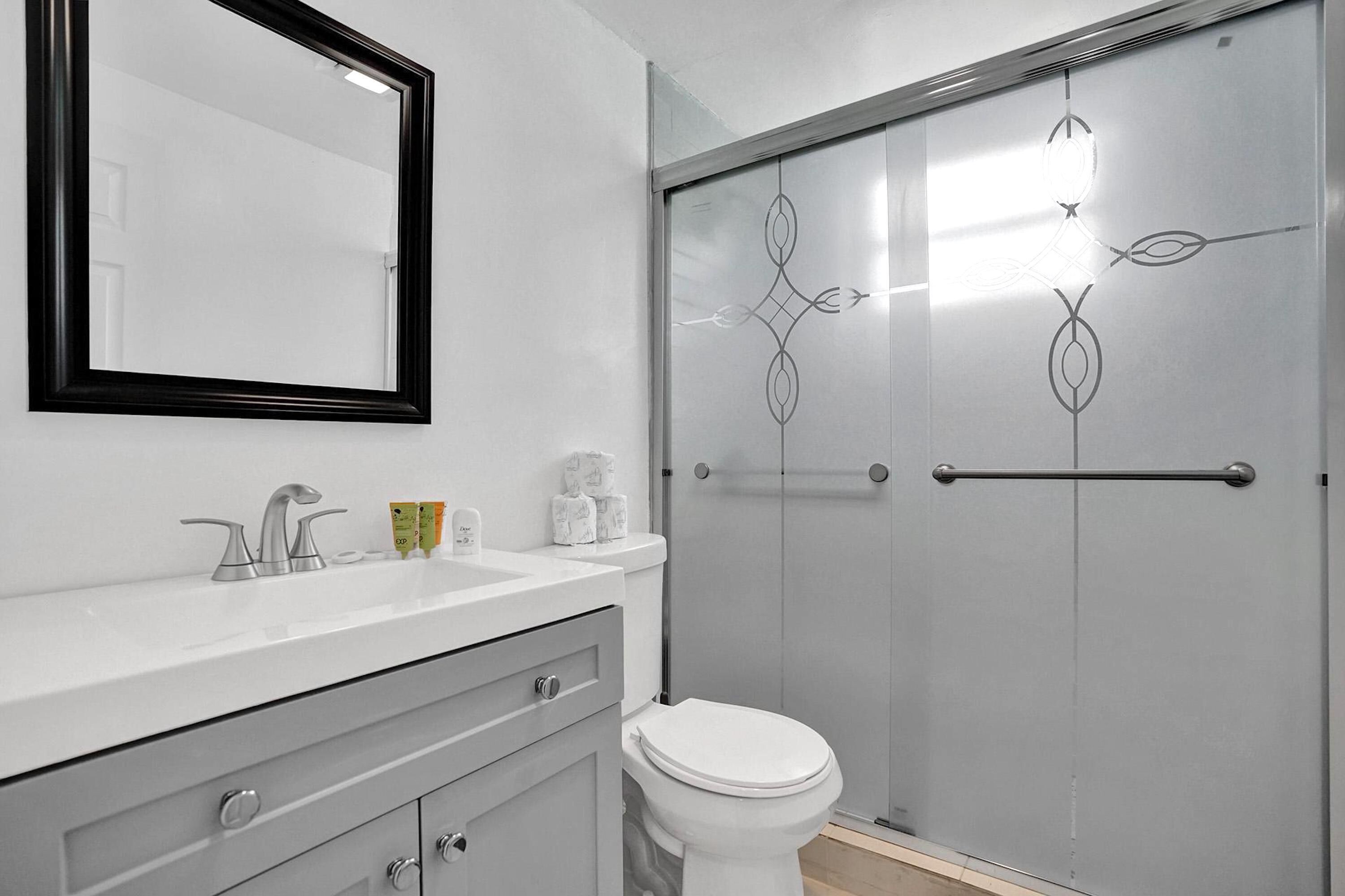 A bathroom with a white sink, a mirror, a toilet, and a shower with a glass door.