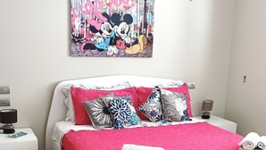 Une chambre moderne avec un lit blanc, une literie rouge et une affiche de Mickey et Minnie Mouse accrochée au mur.