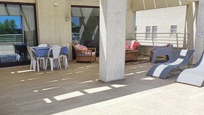 Un espace extérieur ensoleillé, aménagé avec une table et des chaises, un fauteuil en osier et des chaises longues.