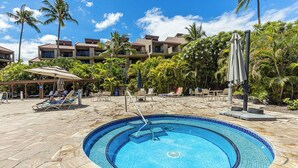 A pool area with lounge chairs, palm trees, and a building with balconies.