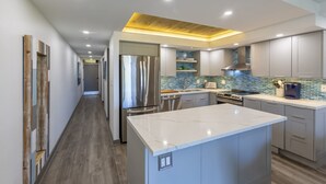 A modern kitchen with a marble island, stainless steel appliances, and a blue-tiled backsplash.