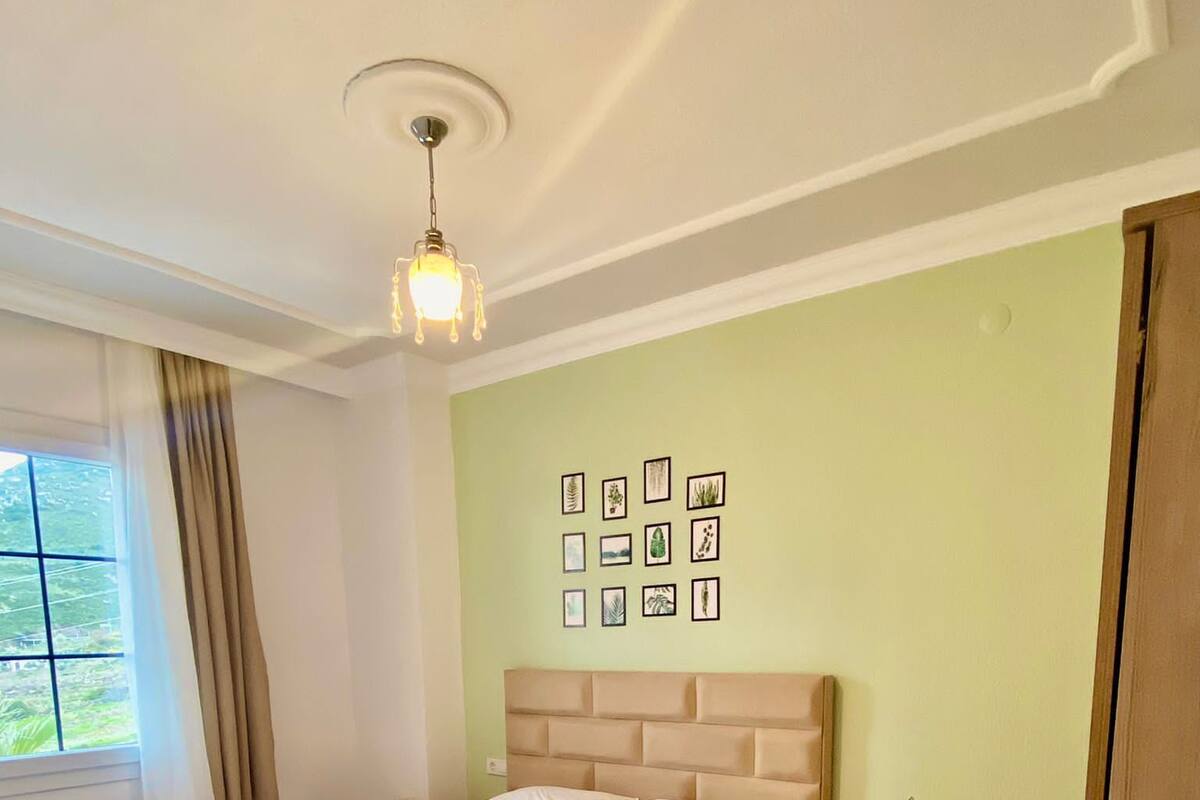 A bedroom with a large bed, a nightstand, a dresser, and a wall of framed pictures.