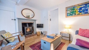A cozy living room with a fireplace, a television, and a comfortable seating area. - 2 Riverside Cottages, Yoxford (Saxmundham)