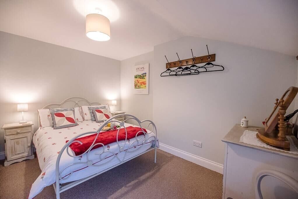 Une chambre à coucher comprenant un lit, des tables de chevet, un porte-manteau fixé au mur et une petite commode.