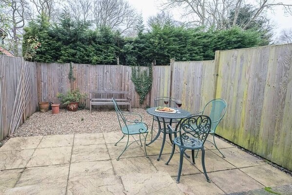 A patio area with a round table and four chairs, surrounded by a wooden fence and potted plants. - 2 Riverside Cottages, Yoxford (Saxmundham)