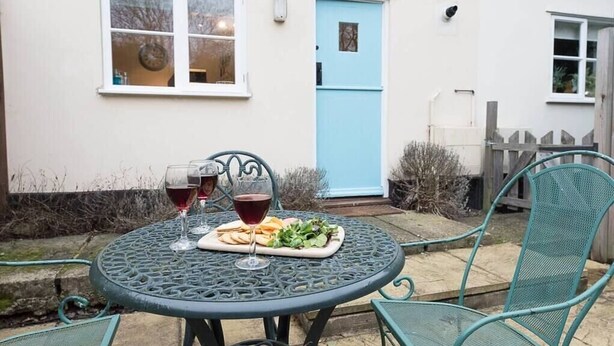 A round metal table with two wine glasses and a plate of food, set against a white building with a blue door. - 2 Riverside Cottages, Yoxford (Saxmundham)
