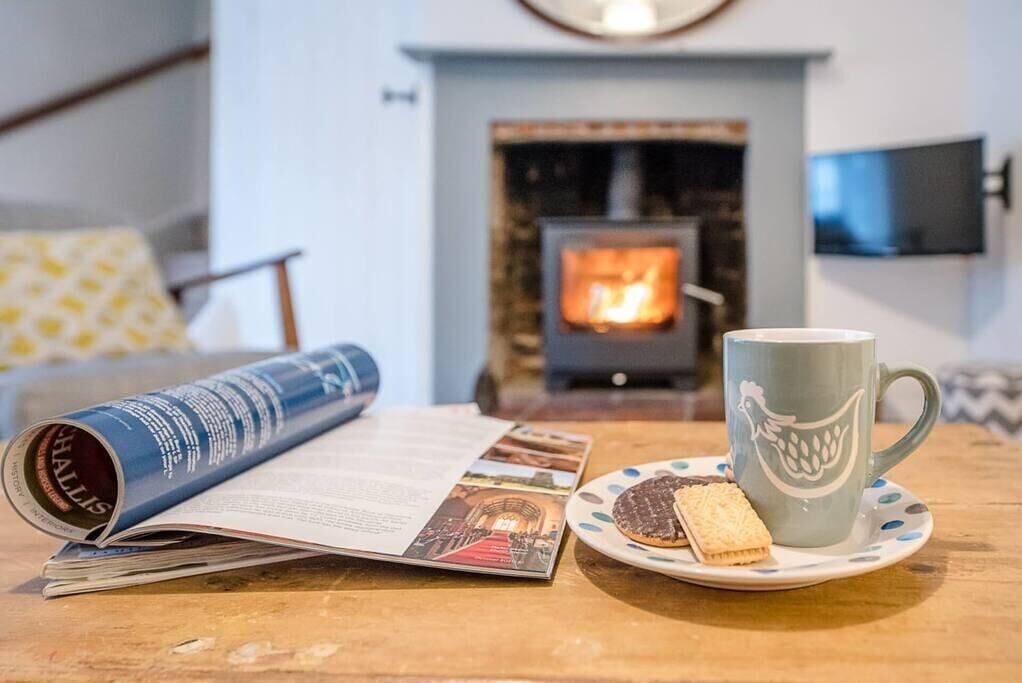 A cozy room with a fireplace, a table with a magazine, a mug, and biscuits.
