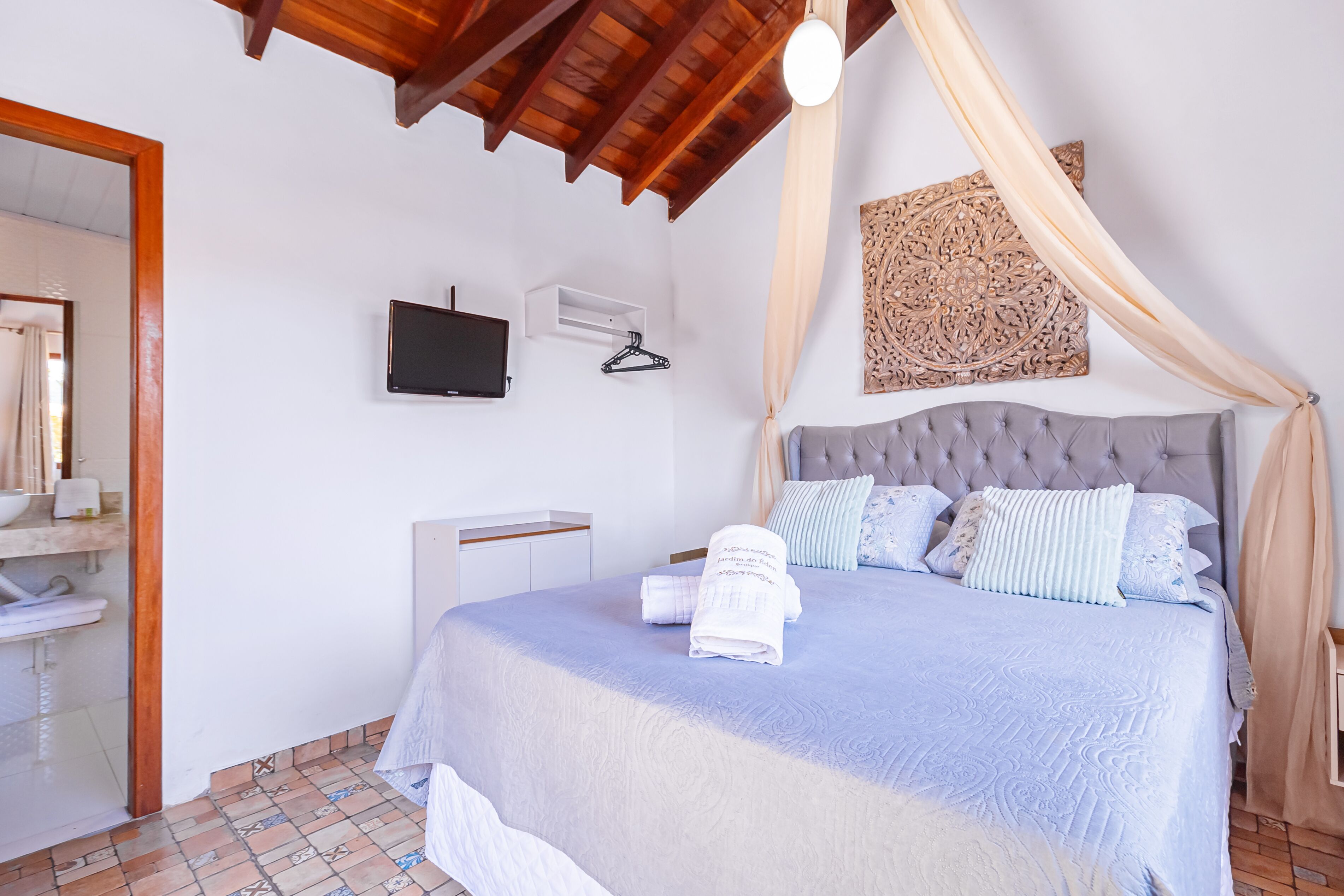 A bedroom with a bed, a TV, a wall-mounted heater, and a bathroom visible through an open door.