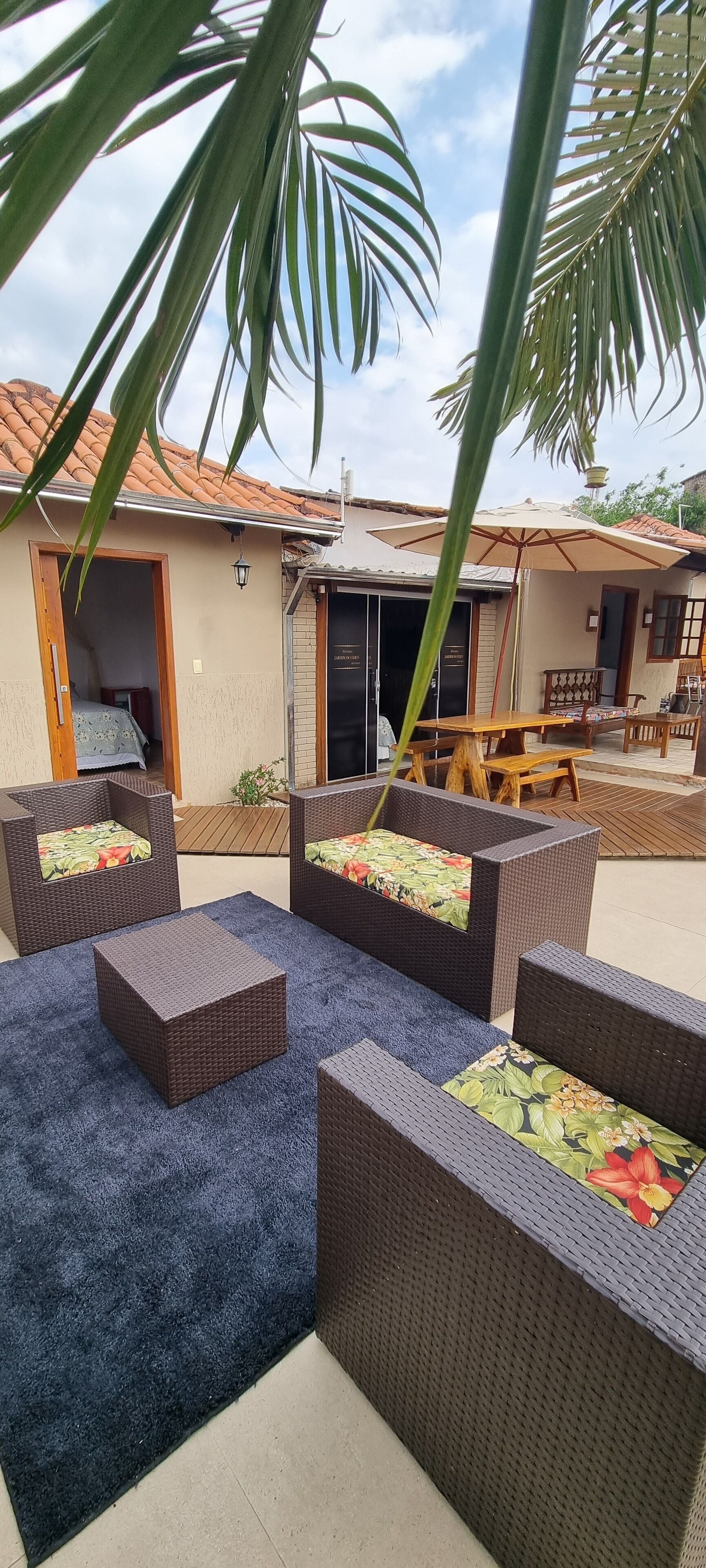 An outdoor seating area with wicker furniture and a blue carpet, a wooden table, and a covered patio.