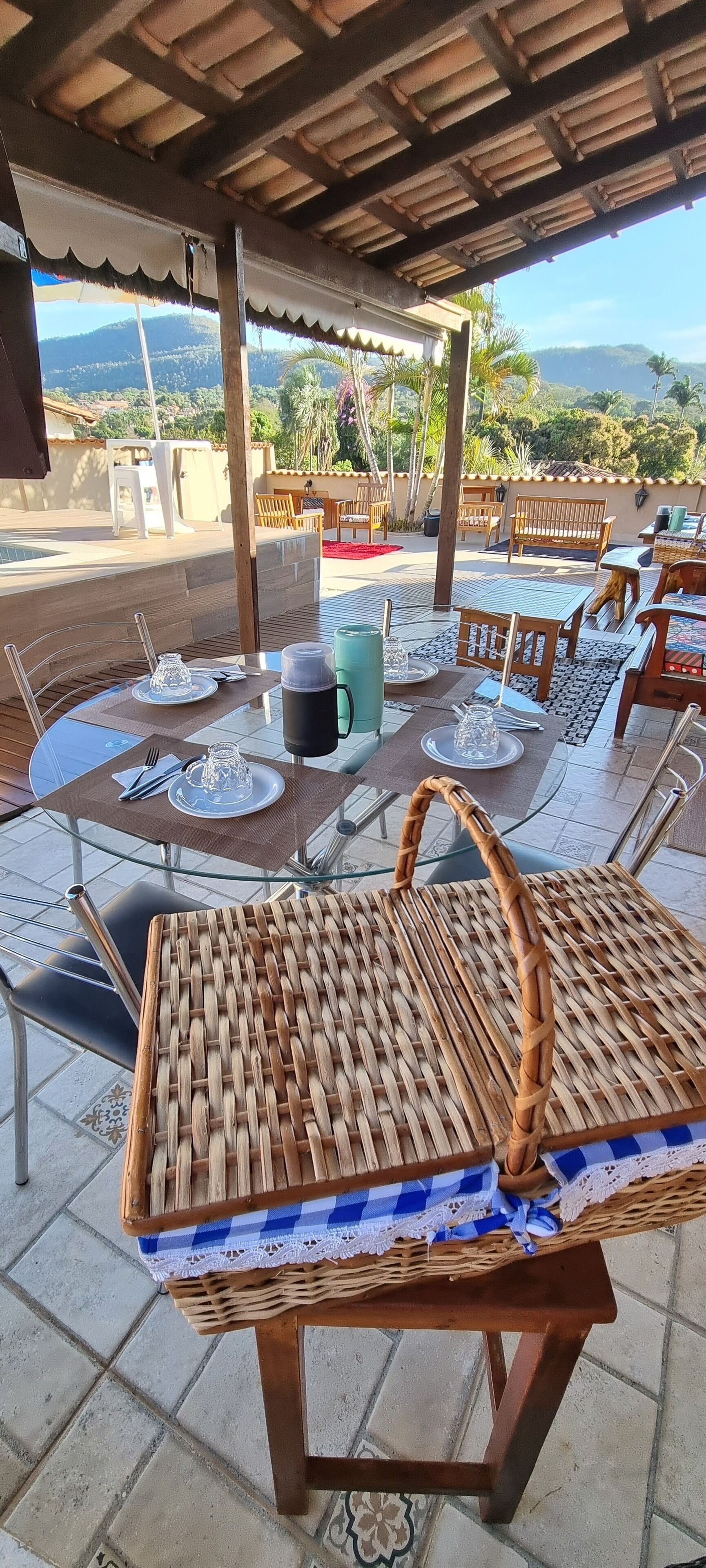 An outdoor dining area with tables set for two, wicker chairs, and a view of the mountains.