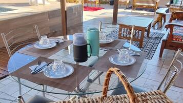 An outdoor dining area with tables set for two, wicker chairs, and a view of the mountains.