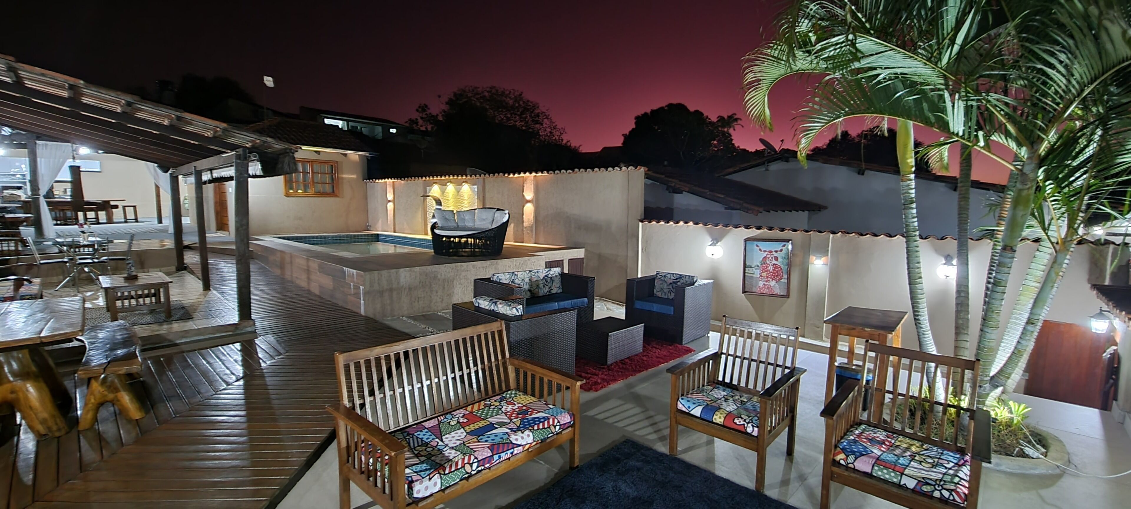 An outdoor patio area with wooden furniture, a pool, and a well-lit ambiance.