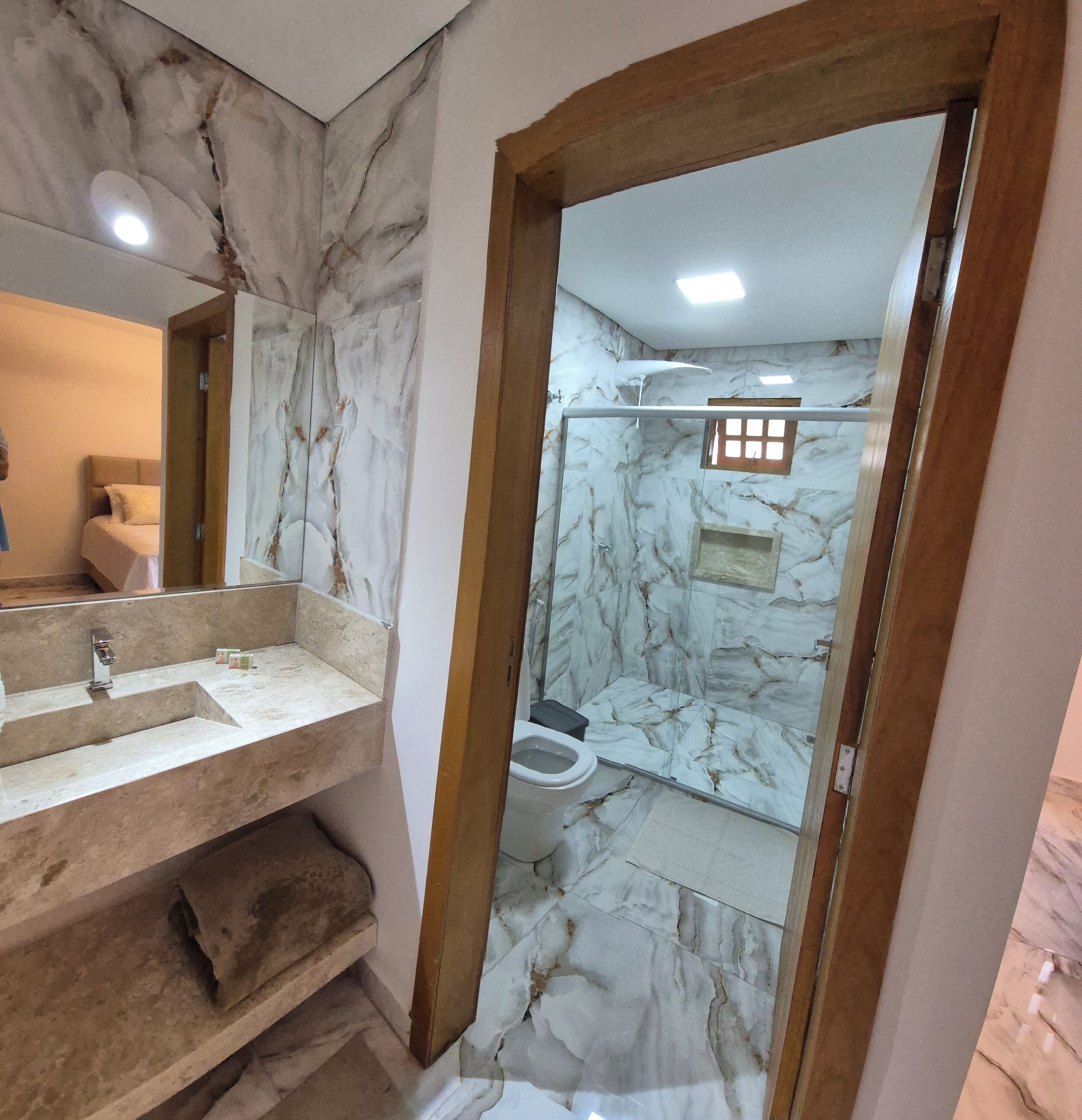 Un baño con paredes de mármol, un lavabo con espejo y zona de ducha.