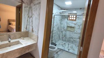 Un baño con paredes de mármol, un lavabo con espejo y zona de ducha.