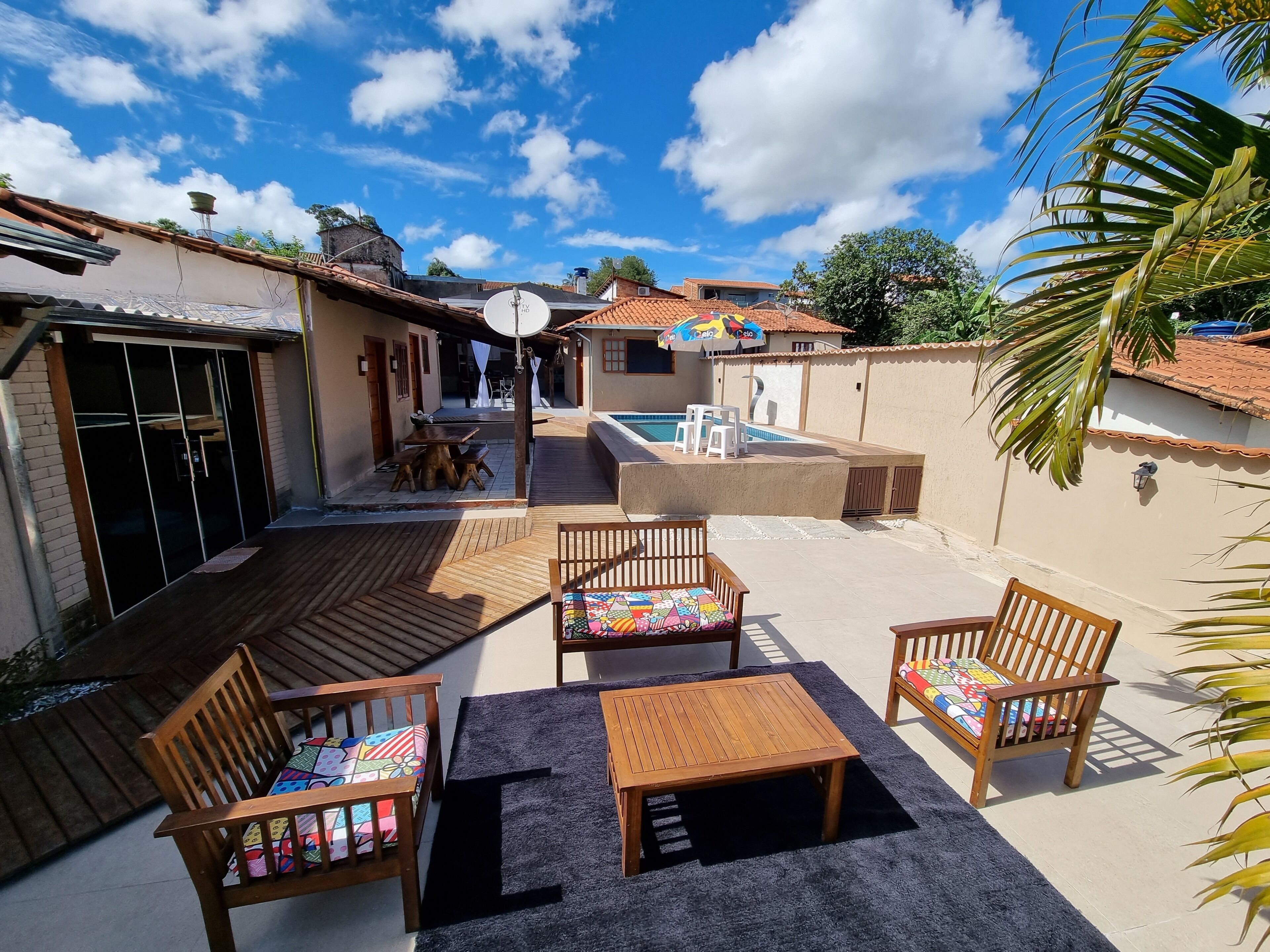 Un patio con muebles de madera, una piscina y un cielo azul despejado.