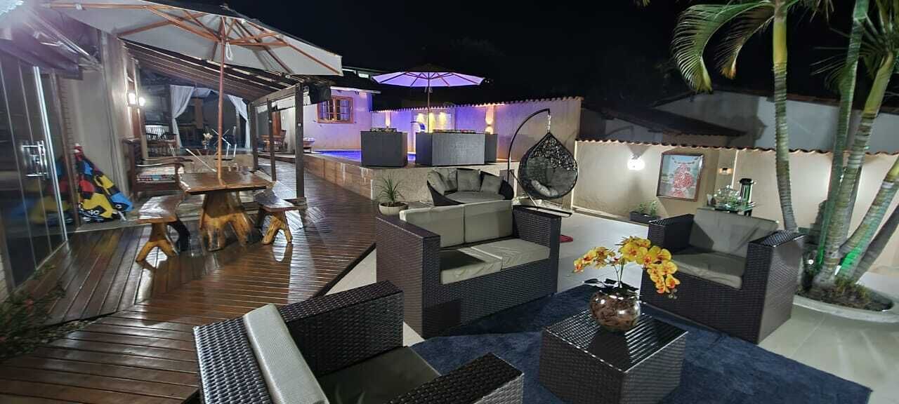 A well-lit outdoor patio area with wicker furniture, a dining table, and a bar area with a pool in the background.