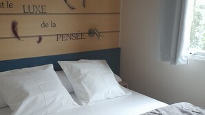 Una cama bien hecha con ropa blanca y cabecera decorada con plumas y texto.