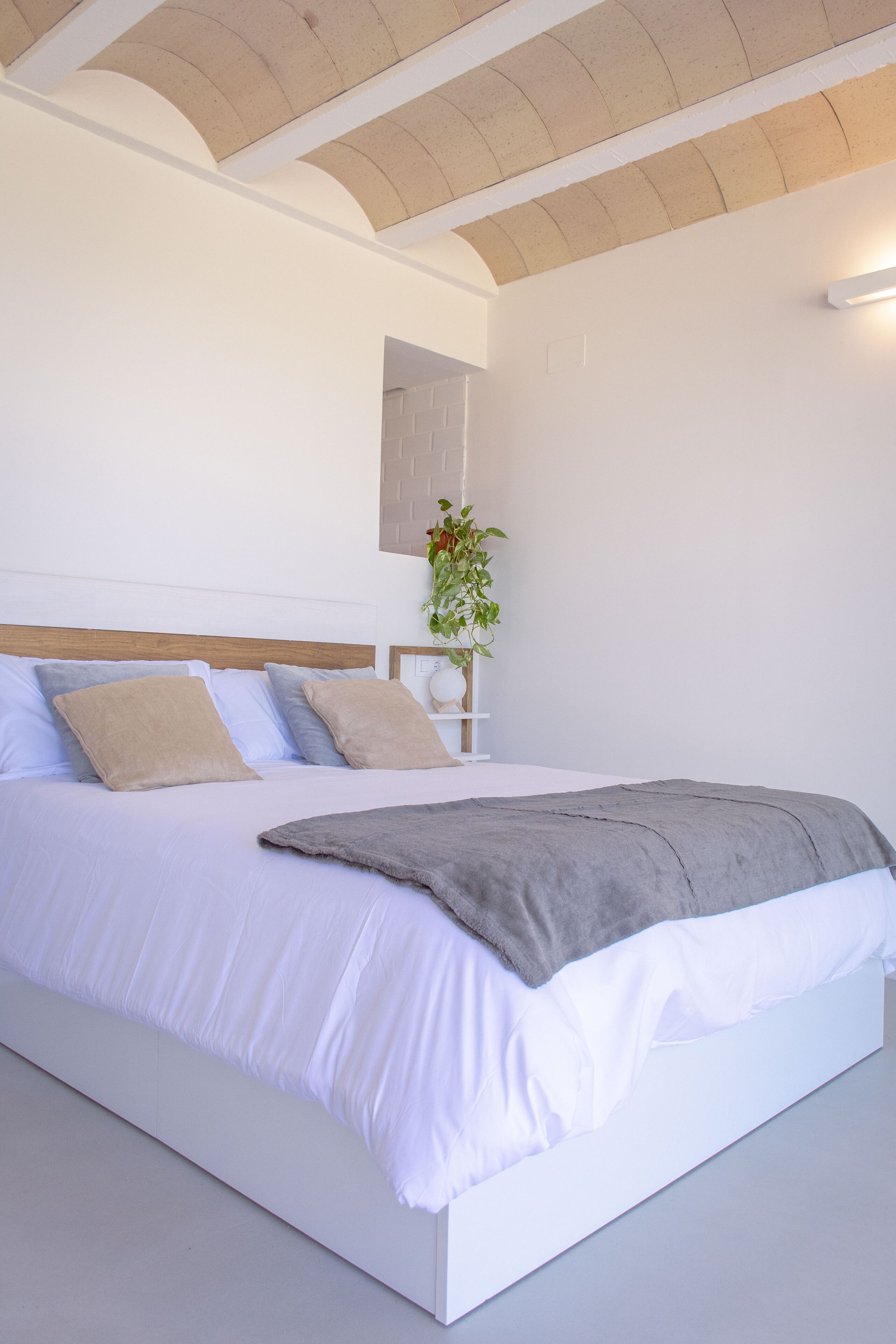 A modern bedroom with a white bed, beige pillows, and a grey throw blanket.