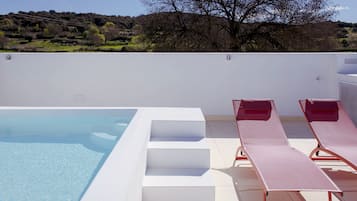 A swimming pool with steps leading into it, two sun loungers, and a view of a hilly landscape.