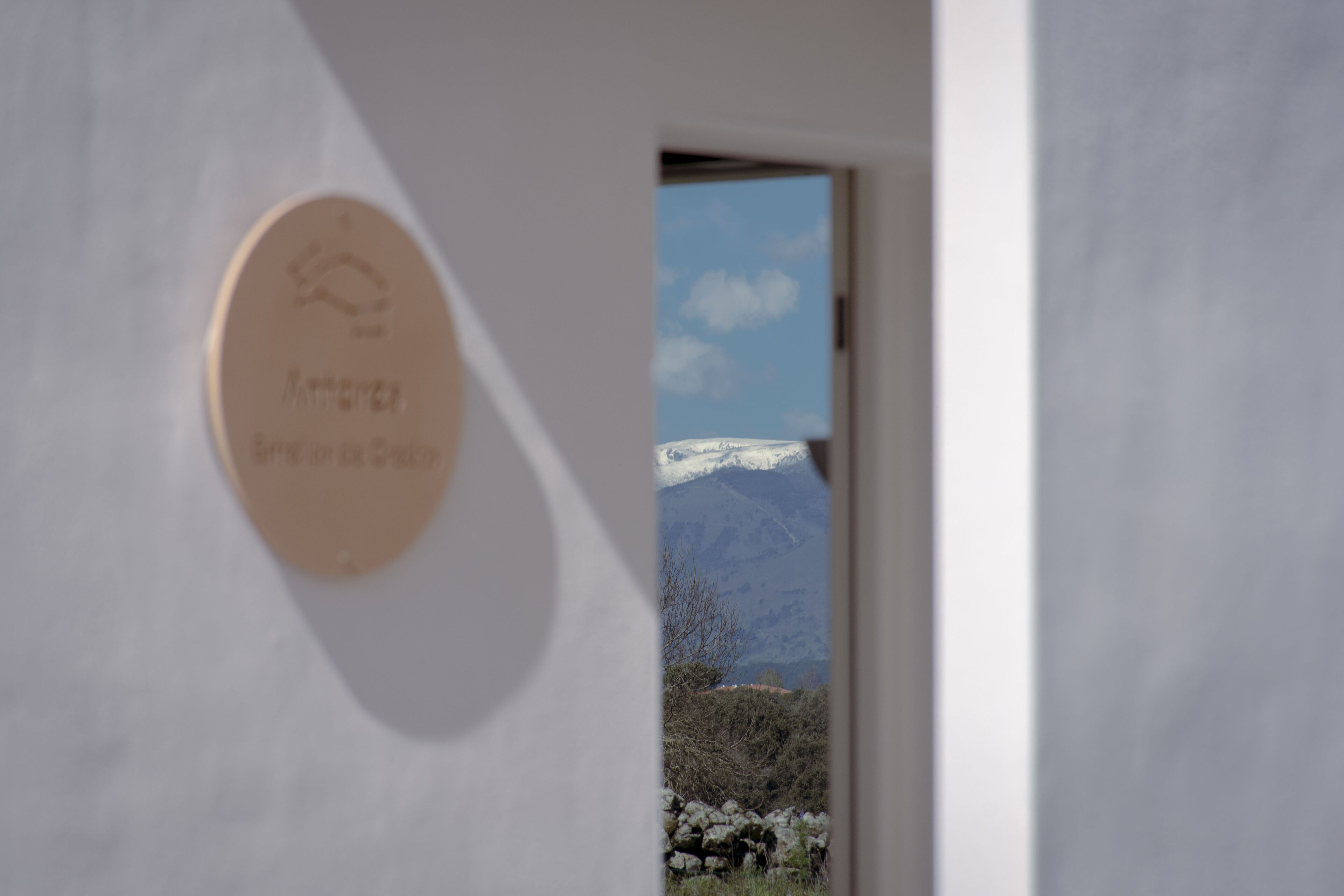 Una puerta con una placa circular y una vista de una montaña nevada a través de un vano abierto.
