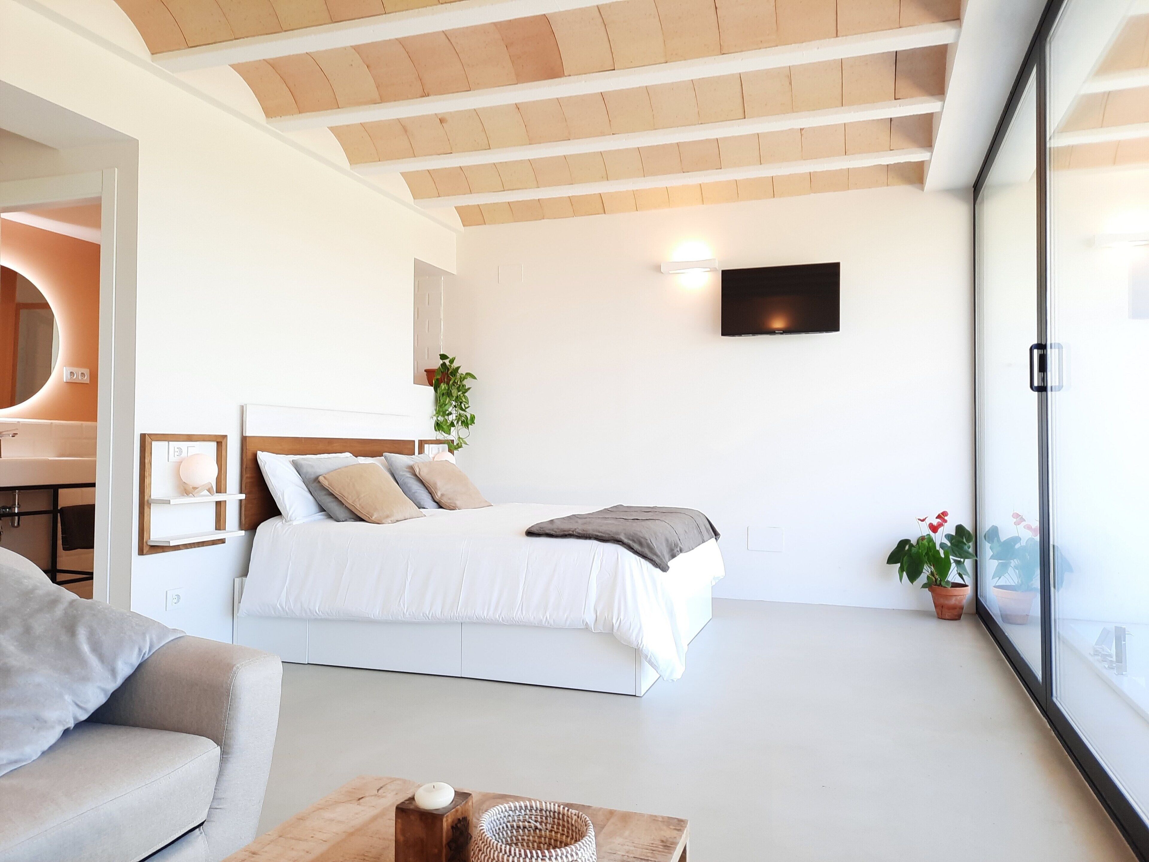 Quarto moderno com cama, TV fixada na parede e janela com vista.