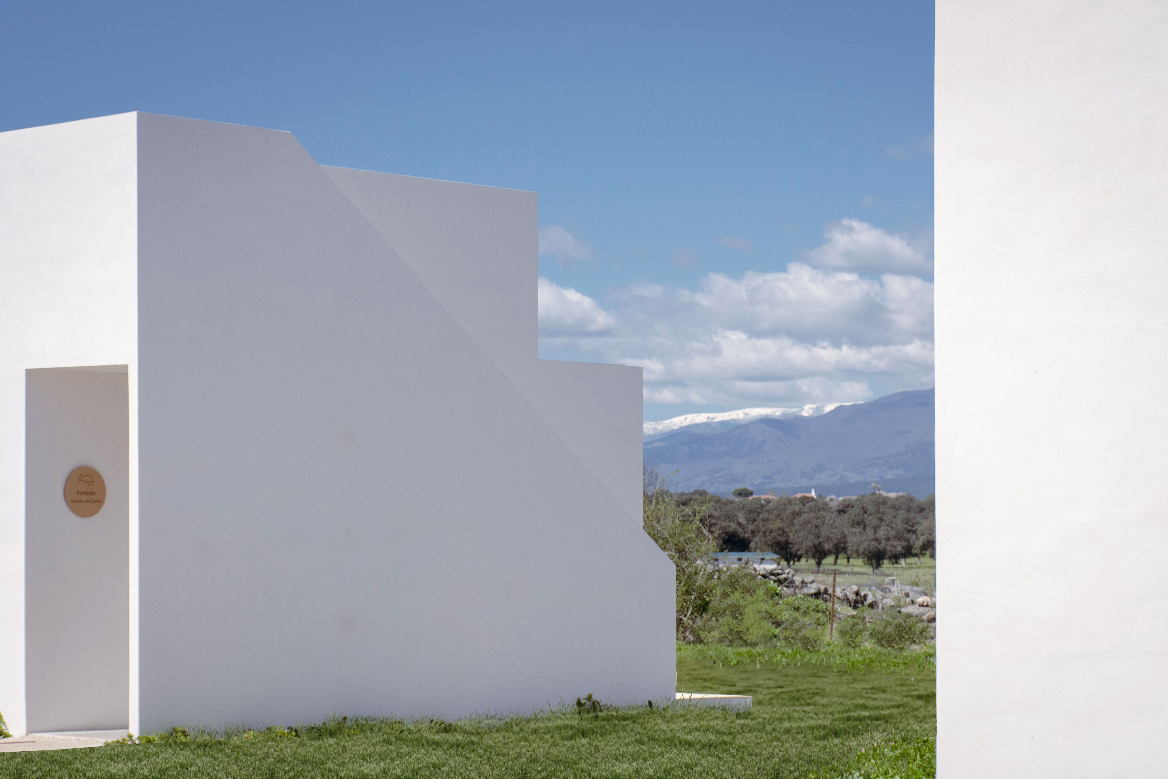 A white building with a plaque, set against a backdrop of mountains and a clear sky.