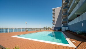 Une piscine sur une terrasse en bois, avec vue sur la mer et un bâtiment moderne doté de balcons.