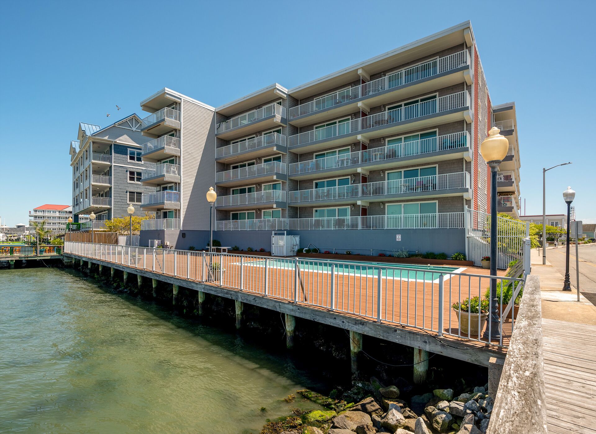Ein mehrstöckiges Hotel mit Balkonen, einem Poolbereich und Blick auf das Wasser.