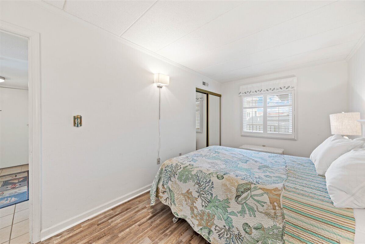 A bedroom with a bed, a nightstand, a lamp, a window with blinds, and a door.