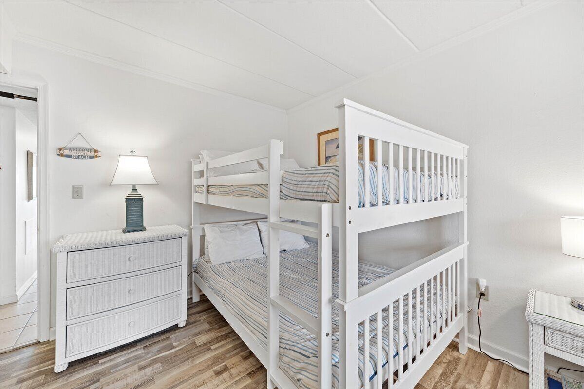Et børneværelse indrettet i hvide farver med køjesenge, en kommode og en lampe.