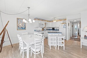 Una cocina luminosa con armarios blancos, una mesa de comedor y un cuadro en la pared.