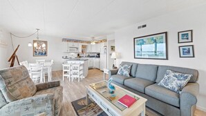 Un salon moderne avec un canapé gris, une table basse et un coin repas avec des chaises blanches.