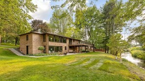 Ein modernes, zweistöckiges Haus mit Balkon, umgeben von üppiger Vegetation und einem kleinen Bach.