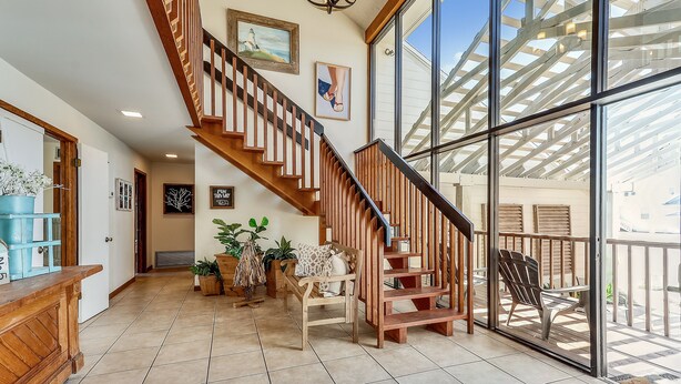 A spacious interior with a wooden staircase, large windows, and a balcony. - Magnolia by the Sea- 5 BR Home with Private Pool on Holiday Isle (Destin)