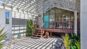 A covered outdoor area with a wooden staircase leading to a balcony, surrounded by greenery and a clear sky. - Magnolia by the Sea- 5 BR Home with Private Pool on Holiday Isle (Destin)