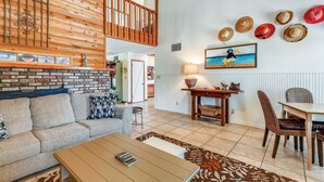 A spacious living area with a wooden ceiling, a dining table with chairs, a sofa, and a fireplace. - Magnolia by the Sea- 5 BR Home with Private Pool on Holiday Isle (Destin)