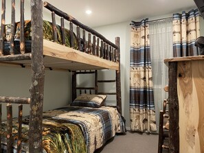 Cozy bedroom with a bunk bed and single bed, featuring a wooden ladder and traditional curtain.