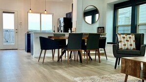 A spacious living area with a dining table, chairs, a sofa, and a kitchen in the background.