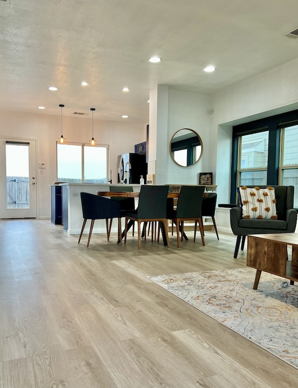 A spacious living area with a dining table, chairs, a sofa, and a kitchen in the background.