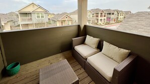 A covered balcony with wicker furniture, a view of neighboring houses, and string lights.