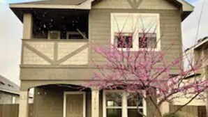 A two-story house with a front porch, a garage, and a small garden with a flowering tree.