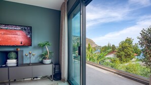 A modern living room with a large flat-screen TV, a potted plant, and a sliding glass door leading to a balcony with a scenic view. - VILLA GRAZIELLA 200 M FROM THE BEACH (Èze)